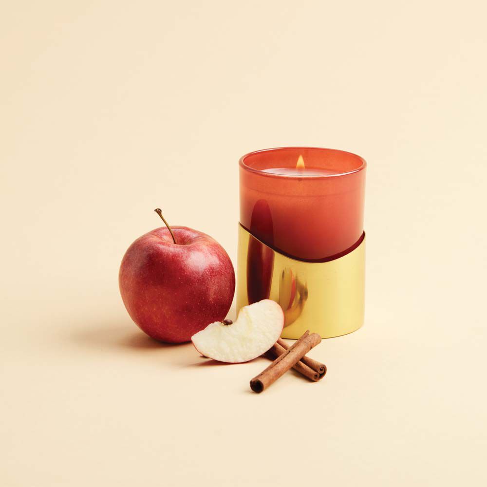 Thymes Simmered Cider Harvest Red Poured Candle with Gold Sleeve next to apple and cinnamon stick image number 1